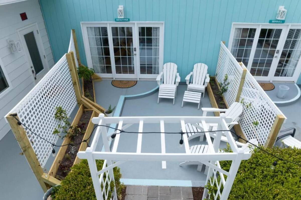 A rooftop terrace with white chairs, a pergola, and a view of a blue building.