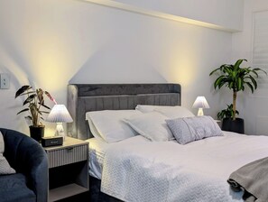 Une chambre à coucher bien rangée, avec un lit, des lampes de chevet, une petite table, une chaise et deux plantes en pot.