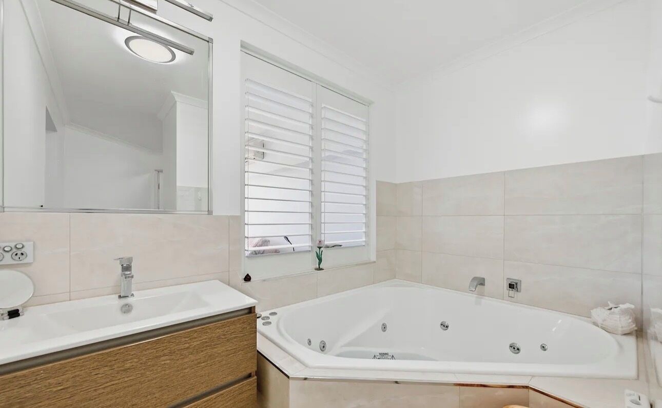 Een moderne badkamer met een groot bad, een wastafel met spiegel en een raam met zonwering.