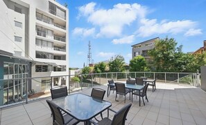 Une terrasse sur le toit, dotée d’un espace extérieur aménagé, d’une balustrade en verre et offrant une vue sur les bâtiments environnants.