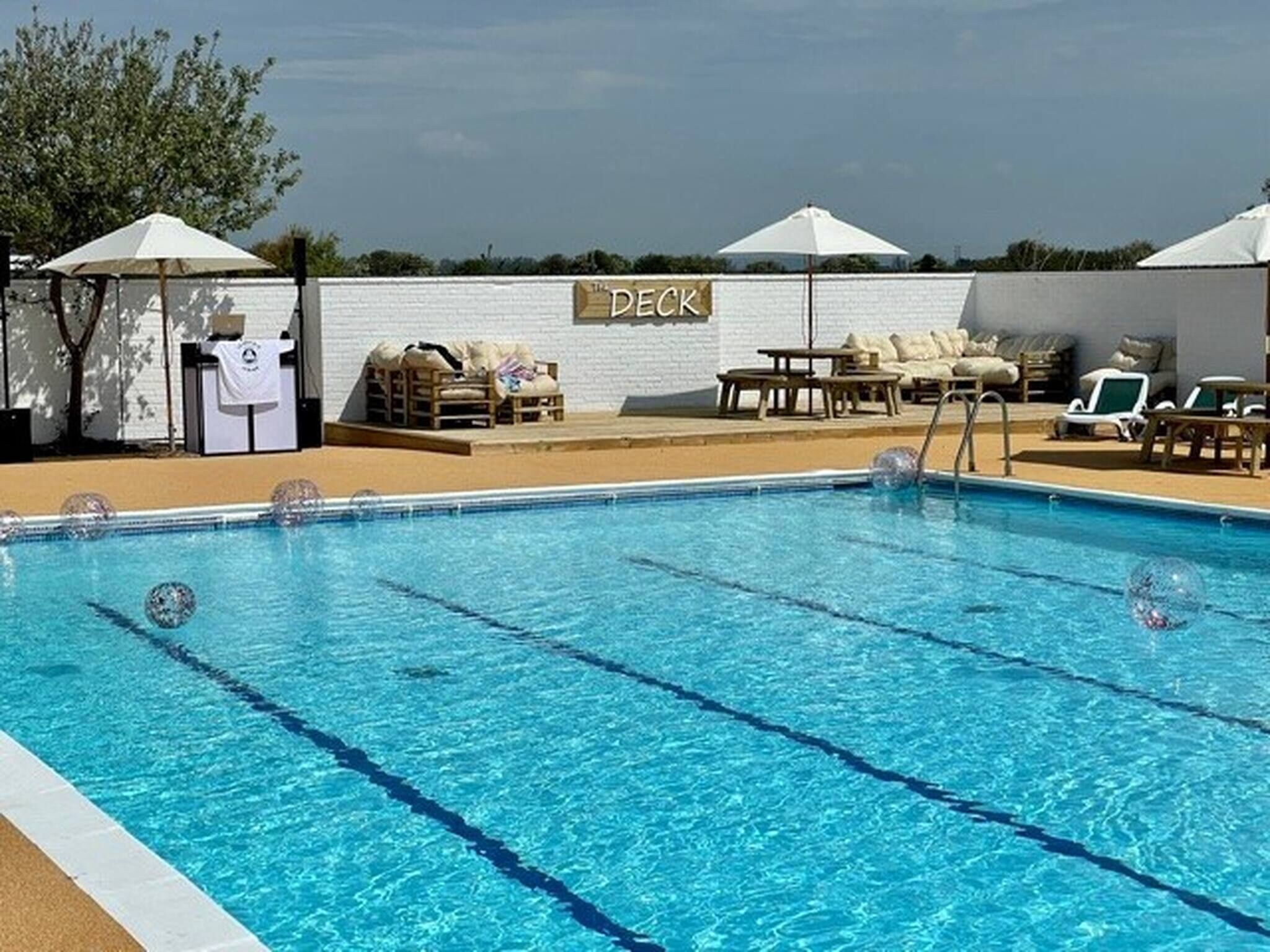 A swimming pool with lounge chairs and umbrellas, a deck area, and a white brick wall.