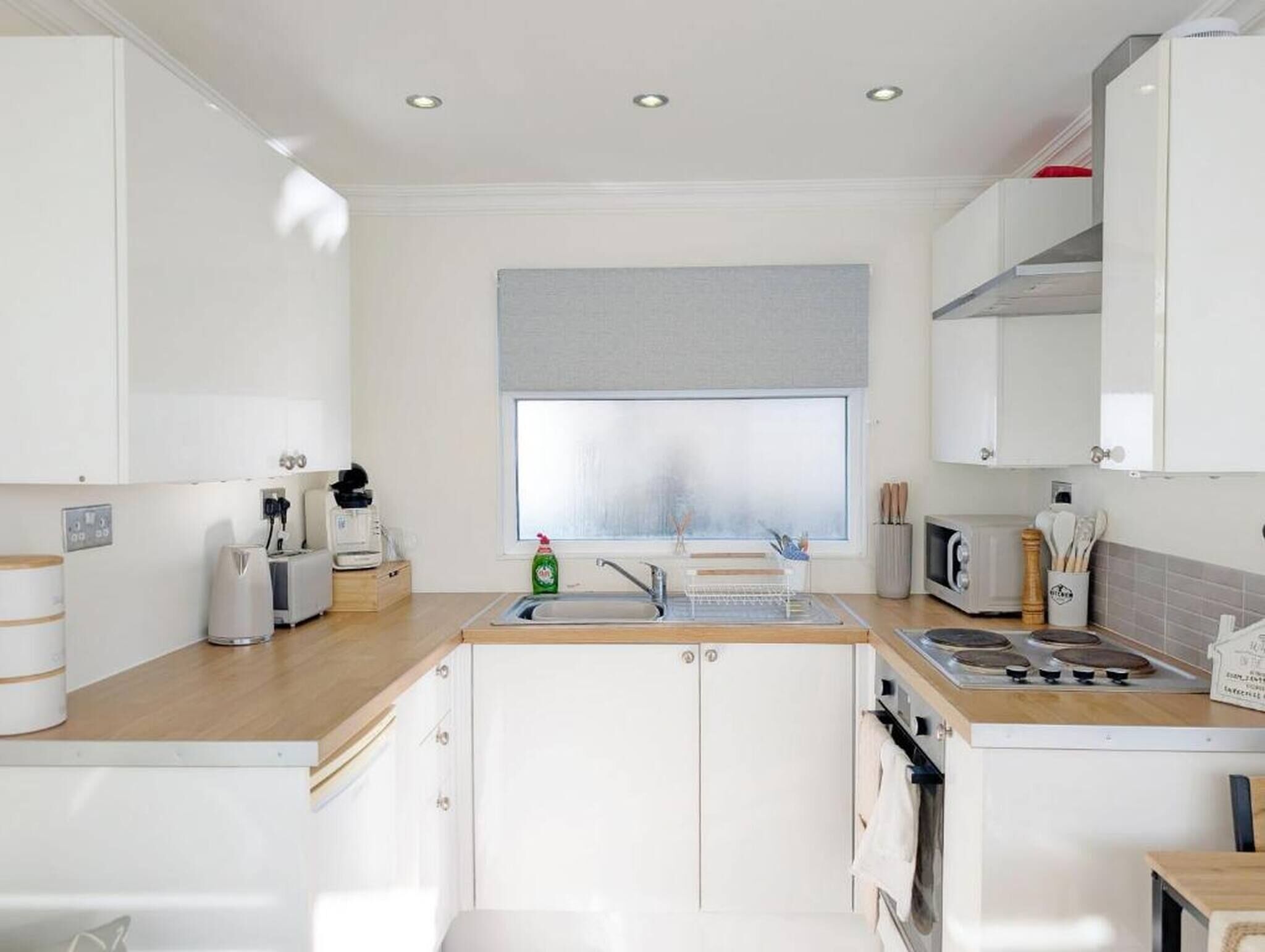 A modern kitchen with white cabinetry, a built-in stove, a sink, and a window with a view.
