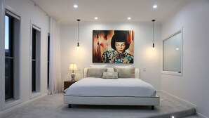 Quarto moderno com uma cama grande, um quadro na parede e uma mesa de cabeceira com abajur.