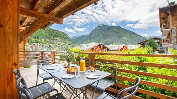 Una terraza de madera con una mesa lista para comer, con vistas a un paisaje montañoso.