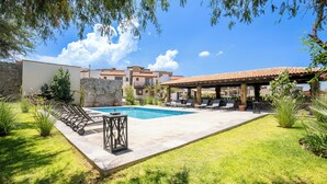 A pool area with lounge chairs and a stone wall. - Modern 3BR Pool & Gym in Nueva Escondida (San Miguel de Allende)