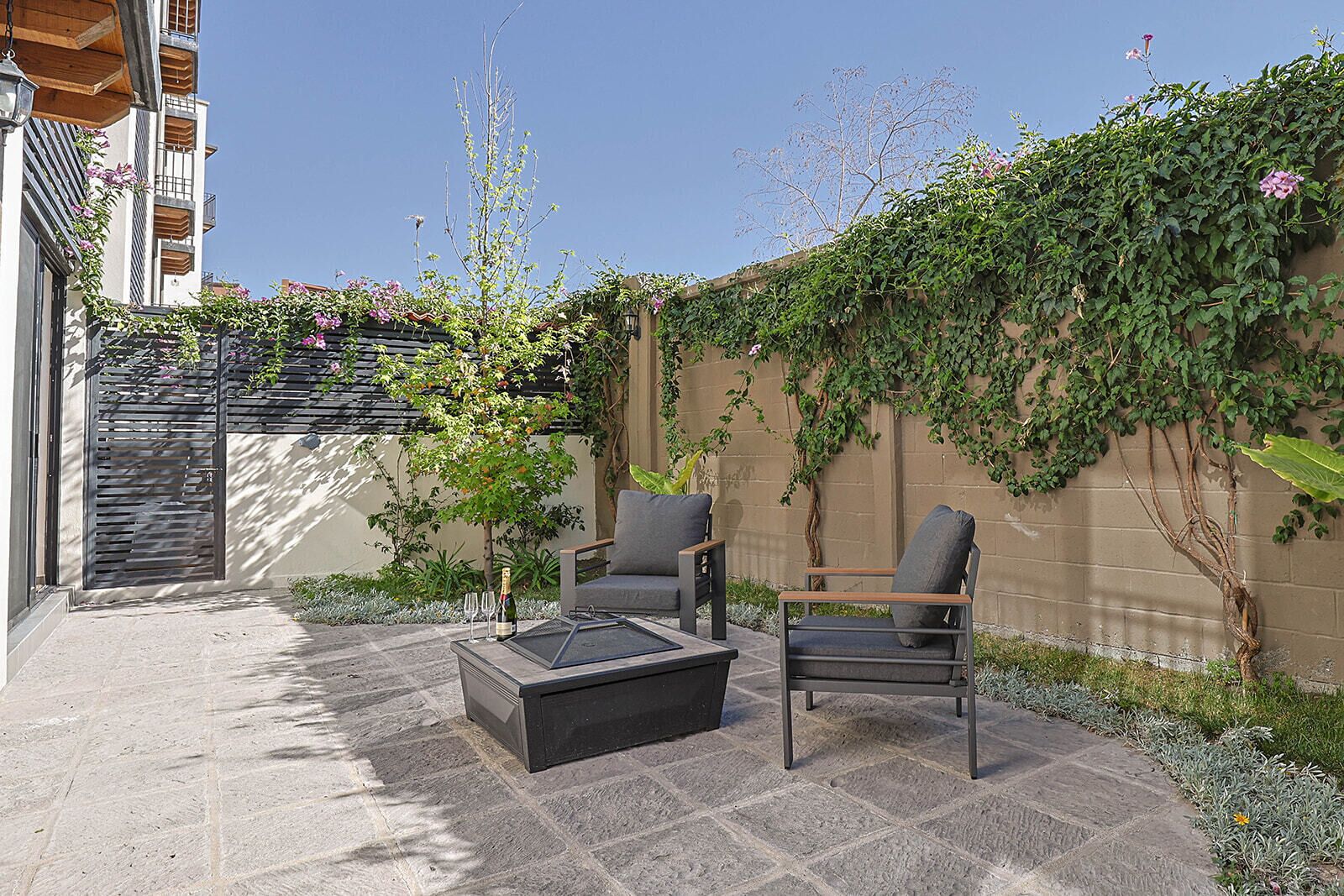 A patio with a table and chairs, a wooden pergola, and a wall covered in ivy.