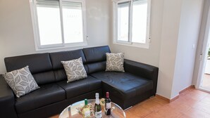 En svart lädersoffa med mönstrade kuddar, ett glasbord med vinflaskor och vinglas, och ett klinkergolv.