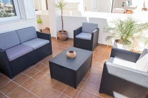 Eine Terrasse mit Korbmöbeln, einem Blumentopf und einem gefliesten Boden.