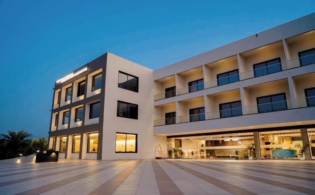 A modern hotel with multiple floors, large windows, and a spacious outdoor area.