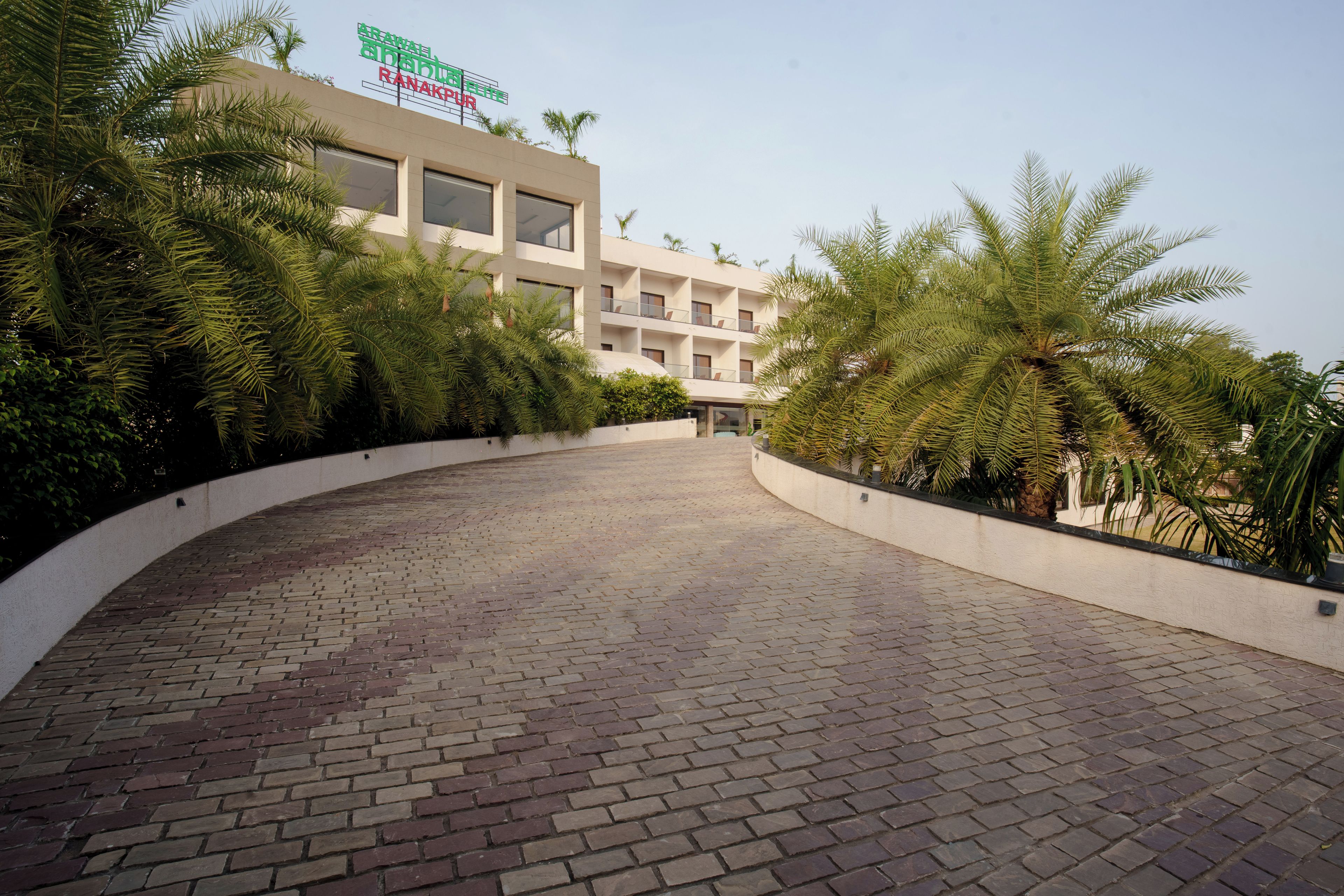 A hotel entrance with a curved brick pathway leading to a building with a sign.