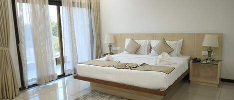 A hotel room with a large bed, two bedside tables, a window with curtains, and a door.
