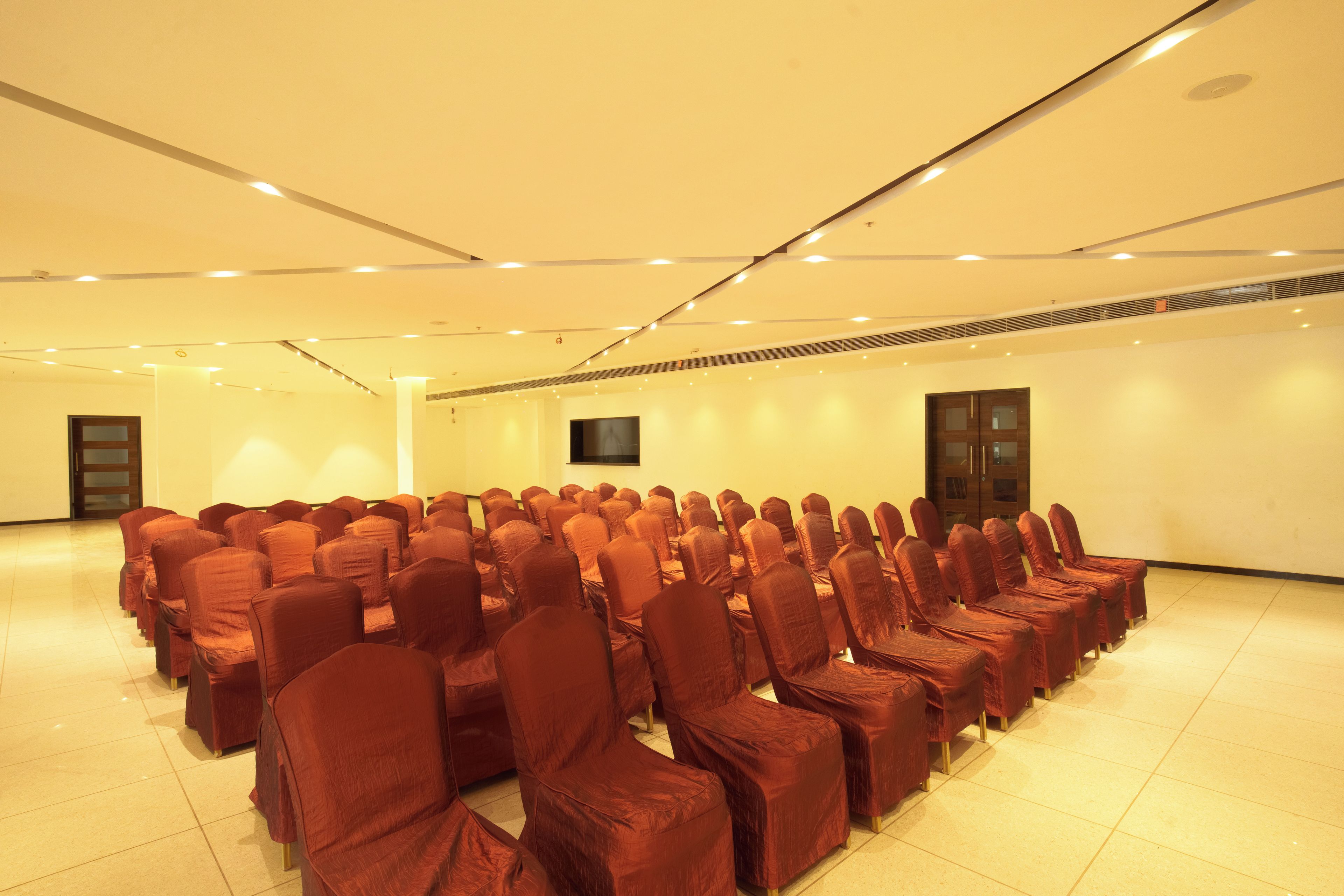 Un salón de conferencias con filas de sillas, un televisor de pantalla plana y una puerta.