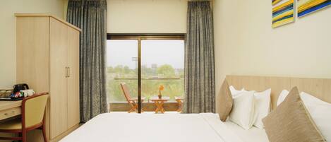 A hotel room with a bed, a desk, and a view of the outdoors.