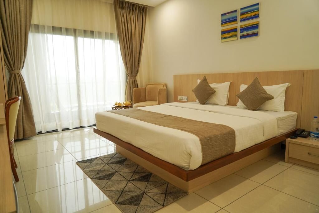 A hotel room with a large bed, a chair, a nightstand, and a painting on the wall.