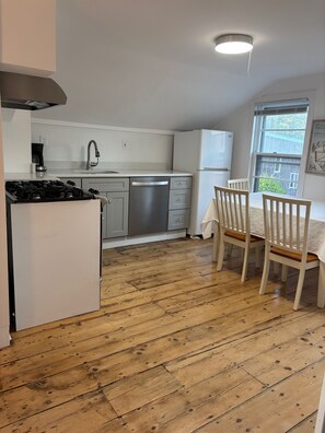 A compact kitchen with a stove, sink, and dishwasher, a dining table with chairs, and a window with a view of greenery. -  fantastic 2-bedroom apartment deck and water view in walk to village Sag Harbor (Sag Harbor)
