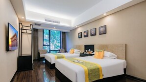 Une chambre d’hôtel avec deux lits, un bureau, une chaise, une fenêtre donnant sur des arbres et des tableaux encadrés au mur.