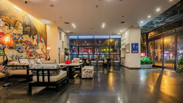 Un hall d’hôtel moderne, doté d’espaces aménagés pour s’asseoir, d’une fresque murale et de grandes fenêtres.