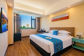 Une chambre d’hôtel avec un grand lit, un bureau, une chaise, une table de chevet et une fenêtre donnant sur des immeubles.