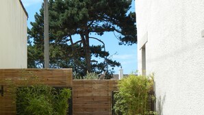 A patio with wooden furniture, a white wall, and a tree in the background. - Nice little house in a good location to forget your car during the vacations. (Paris)