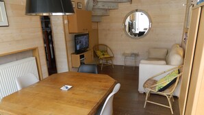 A cozy room with a wooden dining table, chairs, a sofa, a wicker chair, a round mirror, and a television. - Nice little house in a good location to forget your car during the vacations. (Paris)