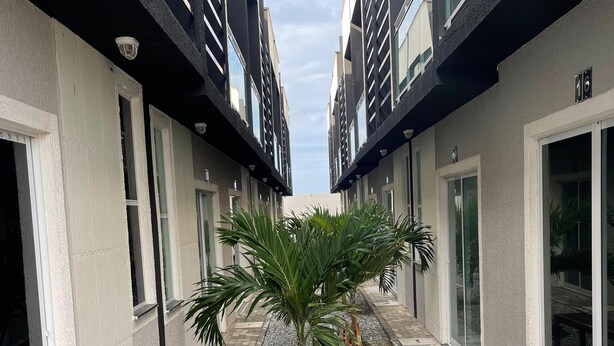 A courtyard with a palm tree, a bench, and a pathway lined with buildings. - House in condominium on the avenue on the beach of Cumbuco close everything 5🏄 (Caucaia)