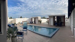 A swimming pool with a tiled edge, surrounded by outdoor seating and potted plants. - House in condominium on the avenue on the beach of Cumbuco close everything 5🏄 (Caucaia)