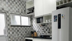 A kitchen with white cabinets, a microwave, a stove, and a refrigerator. - House in condominium on the avenue on the beach of Cumbuco close everything 5🏄 (Caucaia)