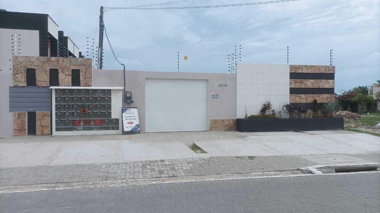 Un edificio con un amplio portón de garaje, un letrero y un pequeño espacio exterior con plantas.