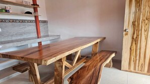Een houten tafel met banken in een ruimte met betegelde vloer en een deur.