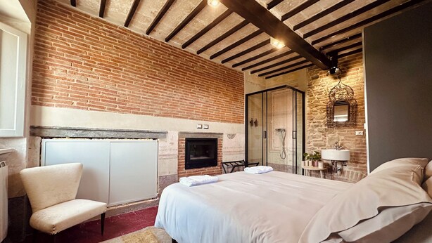 Quarto com parede de tijolos, lareira, cama, poltrona e área de chuveiro.