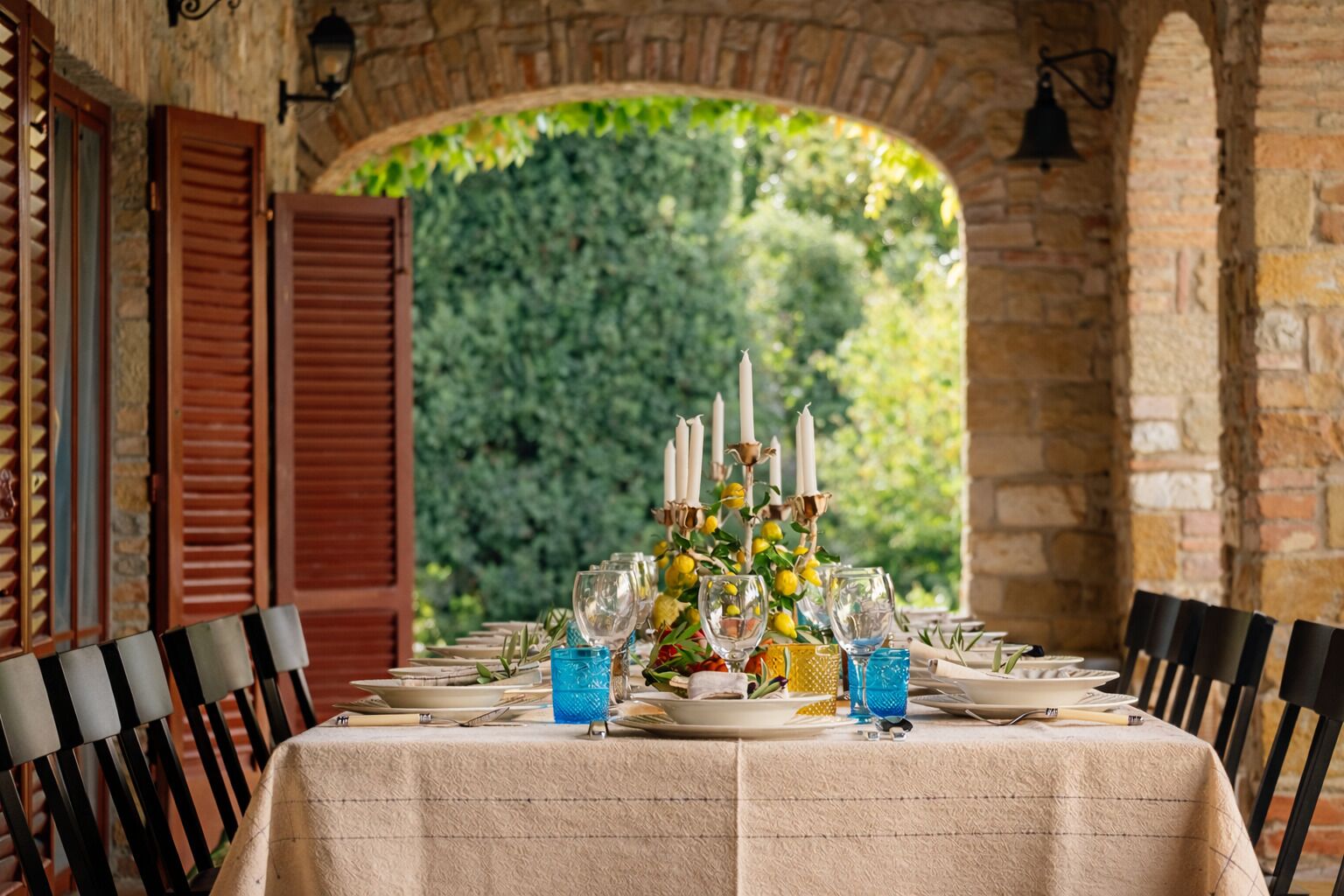 A long dining table set for a meal with candles, glasses, and a centerpiece of flowers.