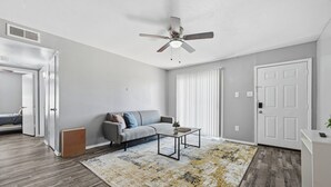 Una sala de estar moderna con un sofá gris, una mesa de centro, un tapete estampado, un ventilador de techo y una puerta blanca.