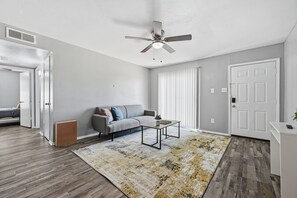 A modern living room with a grey sofa, a coffee table, a patterned rug, a ceiling fan, and a white door. - Charming 2-bedroom 1-bath with modern style appeal (Denton)