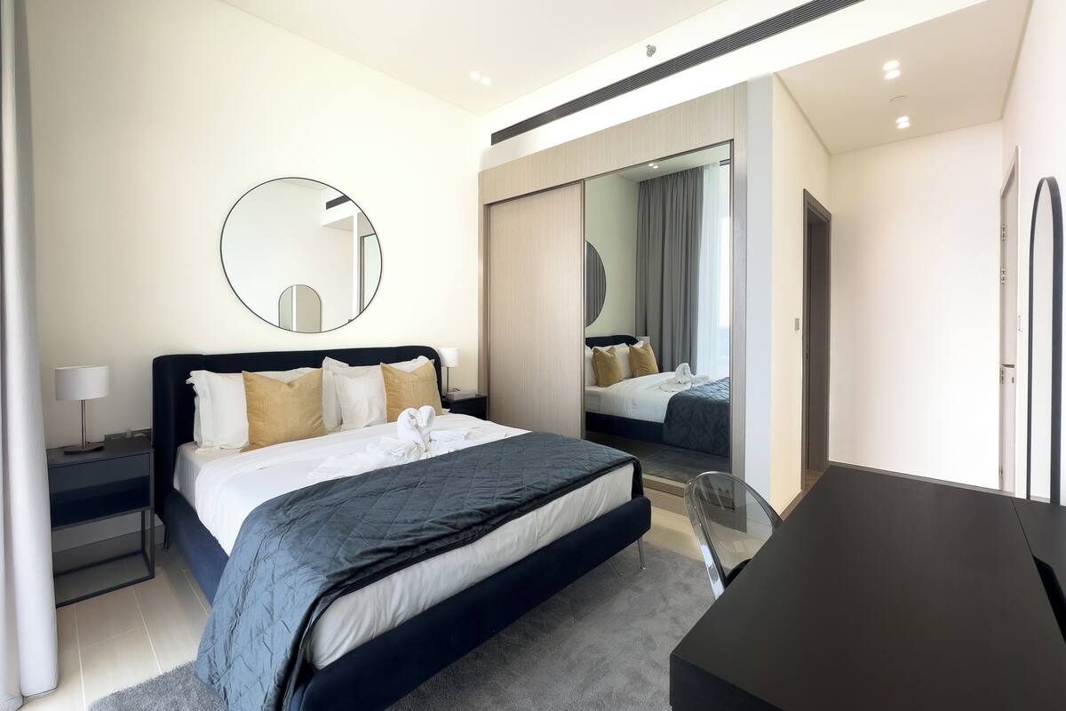 Een moderne hotelkamer met een groot bed, nachtkastjes, een bureau en een spiegel.