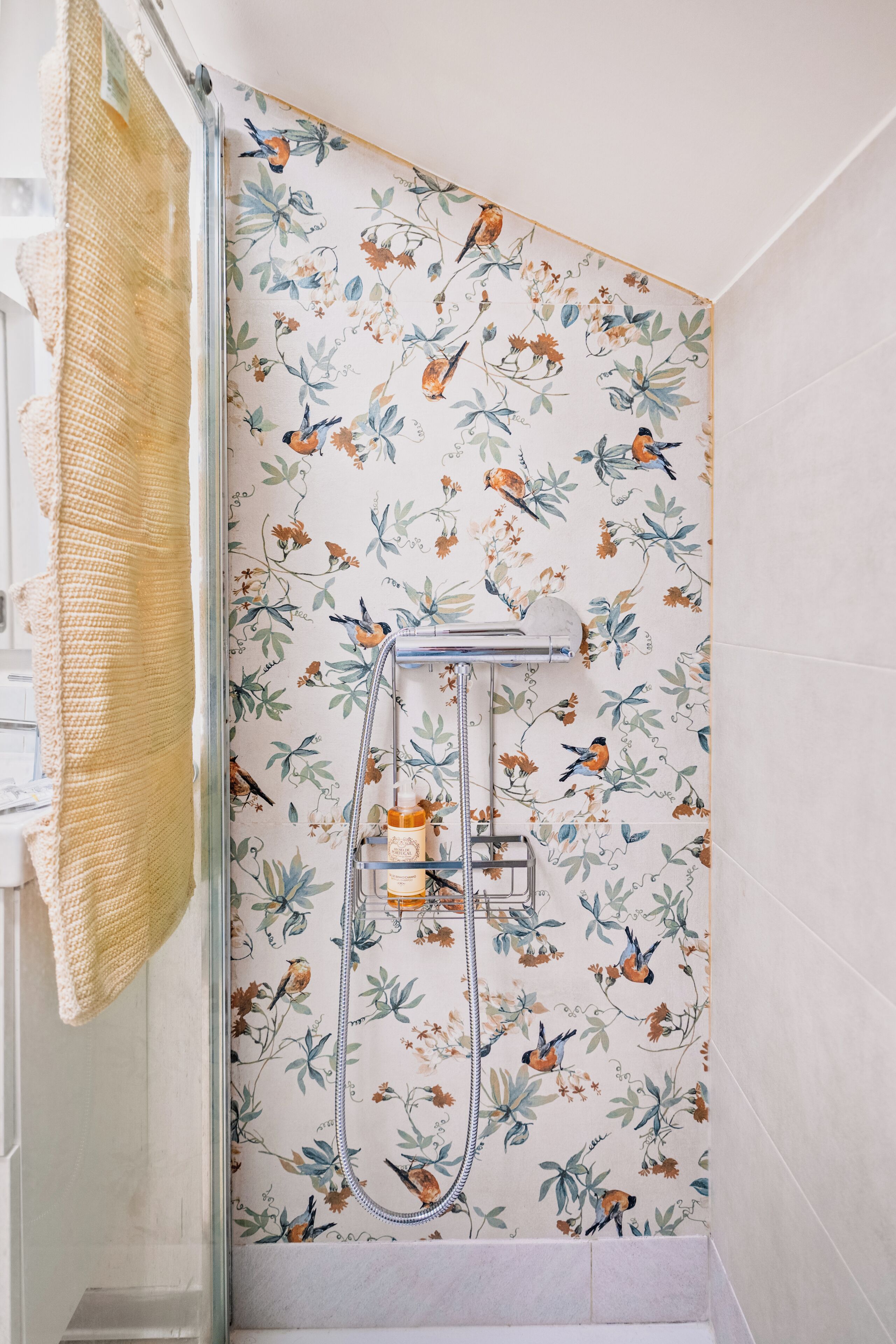 A shower with a floral wallpaper, a towel rack, and a showerhead.