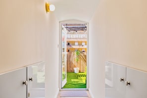 Un pasillo que conduce a una habitación con techo de madera, una pequeña planta en maceta y vistas a un área exterior cercada.
