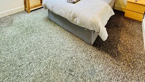 Ein Schlafzimmer mit einem Oberlicht, einem Bett mit einem gestreiften Kopfkissen, einem Nachttisch, einer Lampe und einem Wandbild.