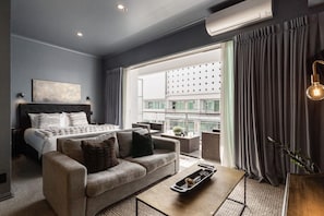 Ein modernes Hotelzimmer mit Bett, Sofa, Couchtisch und Blick auf die Stadtlandschaft.
