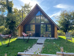A modern wooden cabin with large windows, a patio with seating, and a hammock.