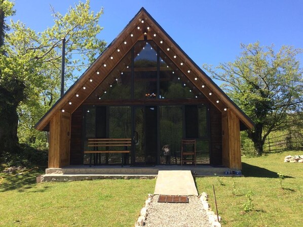 A wooden cabin with a triangular roof, large glass windows, and a wooden bench outside.