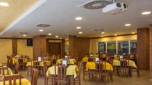 A restaurant with multiple tables covered with yellow tablecloths, wooden chairs, and ceiling-mounted projectors. - Hotel Aréna (Brumov-Bylnice)