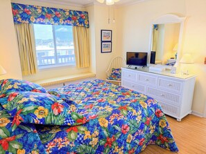 Une chambre à coucher avec un lit, une commode, un téléviseur et une fenêtre avec des rideaux.