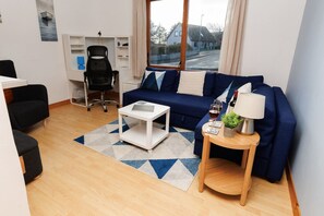 Una sala moderna con un sofá, una mesita blanca, una mesita auxiliar de madera con una lámpara y una silla.