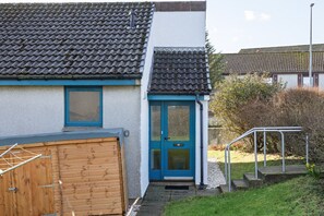 Una casa con puerta azul, puerta de garaje de madera y un pequeño jardín delantero con baranda de metal.