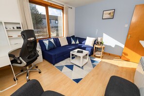 A modern living room with a blue sofa, a white coffee table, and a black office chair.