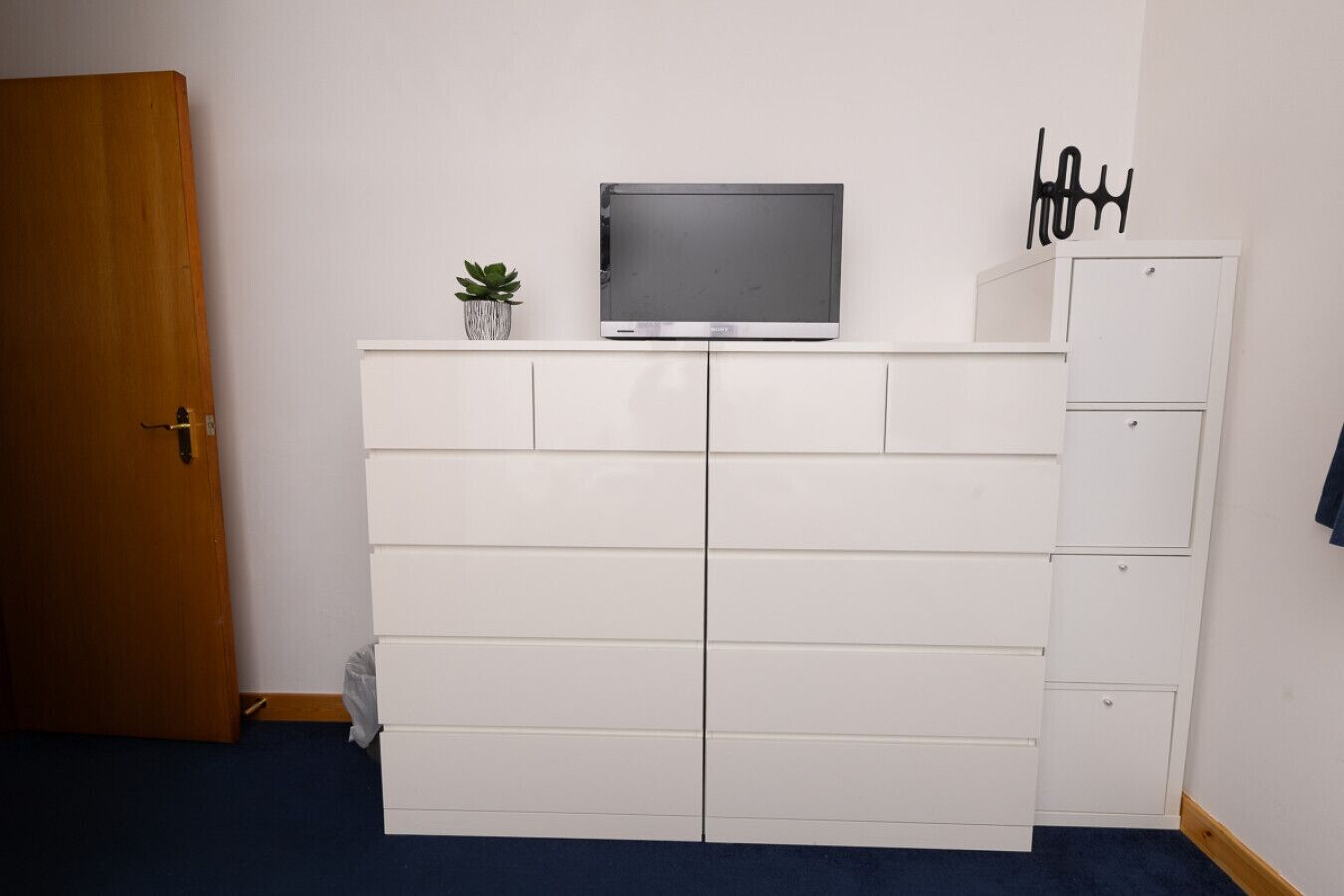 Een kamer met een witte inbouwkast, een televisie bovenop, een kleine plant en een deur.
