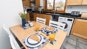 A breakfast setup with croissants, orange juice, and a vase of flowers in a modern kitchen with wooden cabinets and a window.