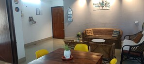 A dining area with a wooden table, yellow chairs, a wicker sofa, and a small round table. - KK HOMES GUWAHATI (Guwahati)
