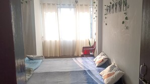 A bedroom with a bed, curtains, a chair, and a wall with a decorative item. - KK HOMES GUWAHATI (Guwahati)