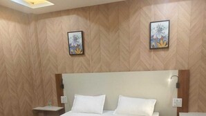 A hotel room with a large bed, wooden flooring, a modern headboard, and two wall-mounted artworks. - Natures Crown Resort (Dehradun)